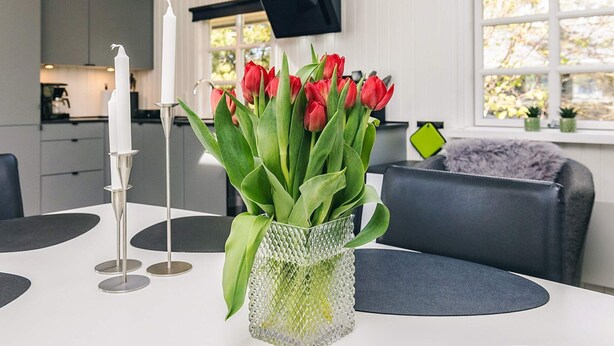 A modern kitchen with white cabinets, a dining table with a vase of red tulips, and a black sofa.