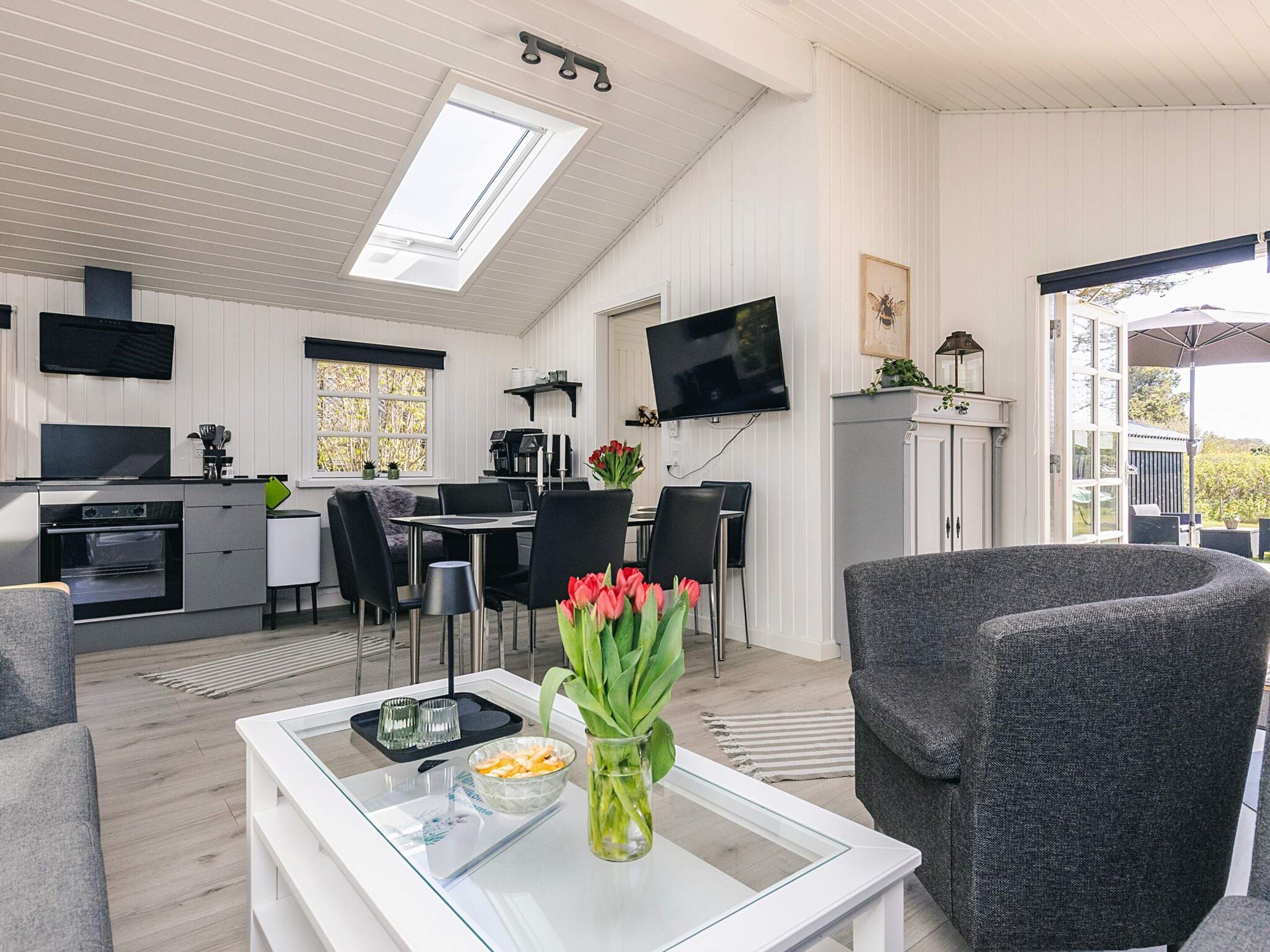 Et moderne køkken med spiseplads, et fladskærms-tv og et hyggeligt opholdsområde med et bord og stole.