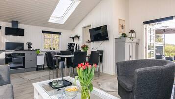 Et moderne køkken med spiseplads, et fladskærms-tv og et hyggeligt opholdsområde med et bord og stole.