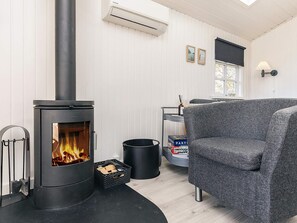 A cozy room with a wood-burning stove, a grey armchair, a small table, and a window with blinds.