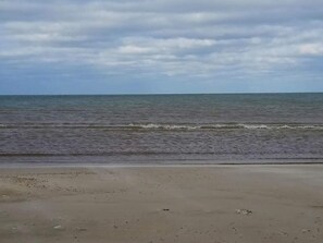 Uma praia com areal arenoso e mar calmo sob um céu nublado.