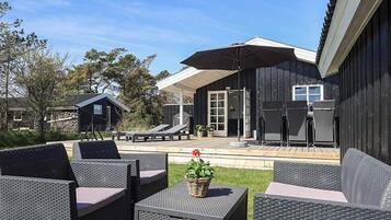 En patio med udendørs møbler, et overdækket siddeområde og en bygning med mørk facade.