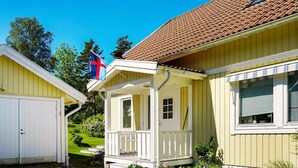Ett gult hus med ett brunt tak täckt av tegelpannor, en vit veranda och en flagga.