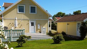 Ett tvåvåningshus med en veranda på framsidan, en liten trädgård och ett rött tegeltak.