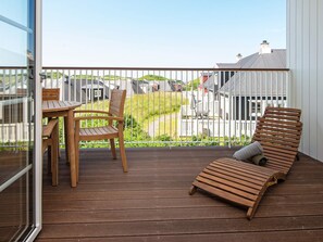 A wooden deck with a table and chairs, a lounge chair, and a view of a white fence and houses.