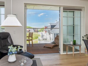A modern living room with a sofa, a coffee table with a vase of flowers, a lamp, and a view of a deck with outdoor furniture. - 4 Star Holiday Home in Ringkobing (Ringkobing)