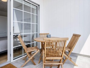 Une table et des chaises en bois sont disposées sur un balcon, près d’une porte-fenêtre coulissante.