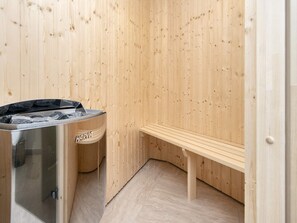 A sauna room with a bench, a sauna heater, and a trash bin. - 4 Star Holiday Home in Ringkobing (Ringkobing)