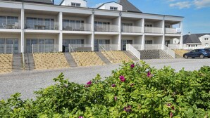 A multi-story hotel with balconies, a parking area, and a garden with purple flowers. - 4 Star Holiday Home in Ringkobing (Ringkobing)