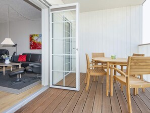 Een open glazen schuindeur leidt naar een houten terras met een ronde houten tafel en stoelen.