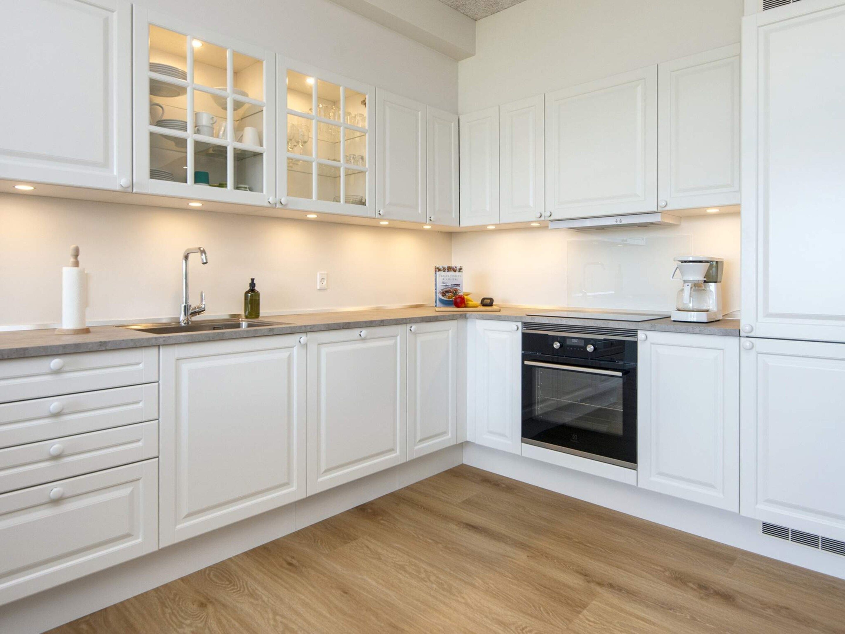 A modern kitchen with white cabinetry, a built-in oven, and a countertop with a coffee maker.
