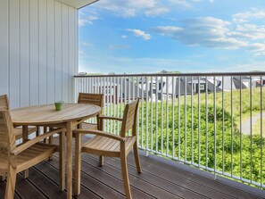 A wooden deck with a round table and chairs, a white railing, and a view of houses and greenery. - 4 Star Holiday Home in Ringkobing (Ringkobing)