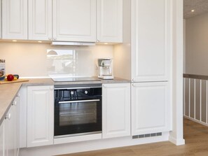 A kitchen with white cabinetry, a built-in oven, and a coffee maker on the countertop. - 4 Star Holiday Home in Ringkobing (Ringkobing)