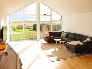 A modern living room with a large window, a dark grey sofa, a small round table, and a beige rug. - 8 Person Holiday Home in Veslos (Vesløs)