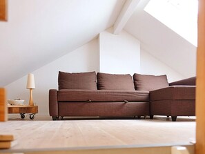 A modern loft bedroom with a brown sectional sofa, a small wooden side table, and a lamp. - 8 Person Holiday Home in Veslos (Vesløs)
