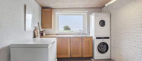 A compact kitchen with a washing machine, wooden cabinets, a window, and a tiled floor.