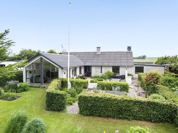 A modern house with a large glass front, a patio with outdoor furniture, and a well-maintained garden.