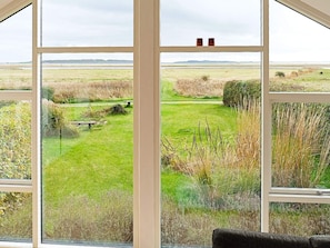 Ein Zimmer mit großen Fenstern, das einen Blick auf ein grasbewachsenes Feld und die ferne Landschaft bietet.