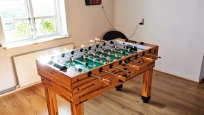 Una mesa de fútbol de mesa en una habitación con suelo de madera, un dardo en la pared y una ventana que deja entrar luz natural.