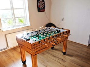 A foosball table in a room with wooden flooring, a dartboard on the wall, and a window providing natural light. - 8 Person Holiday Home in Veslos (Vesløs)