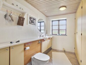 A bathroom with a wooden vanity, a toilet, a sink, a mirror, and a window.
