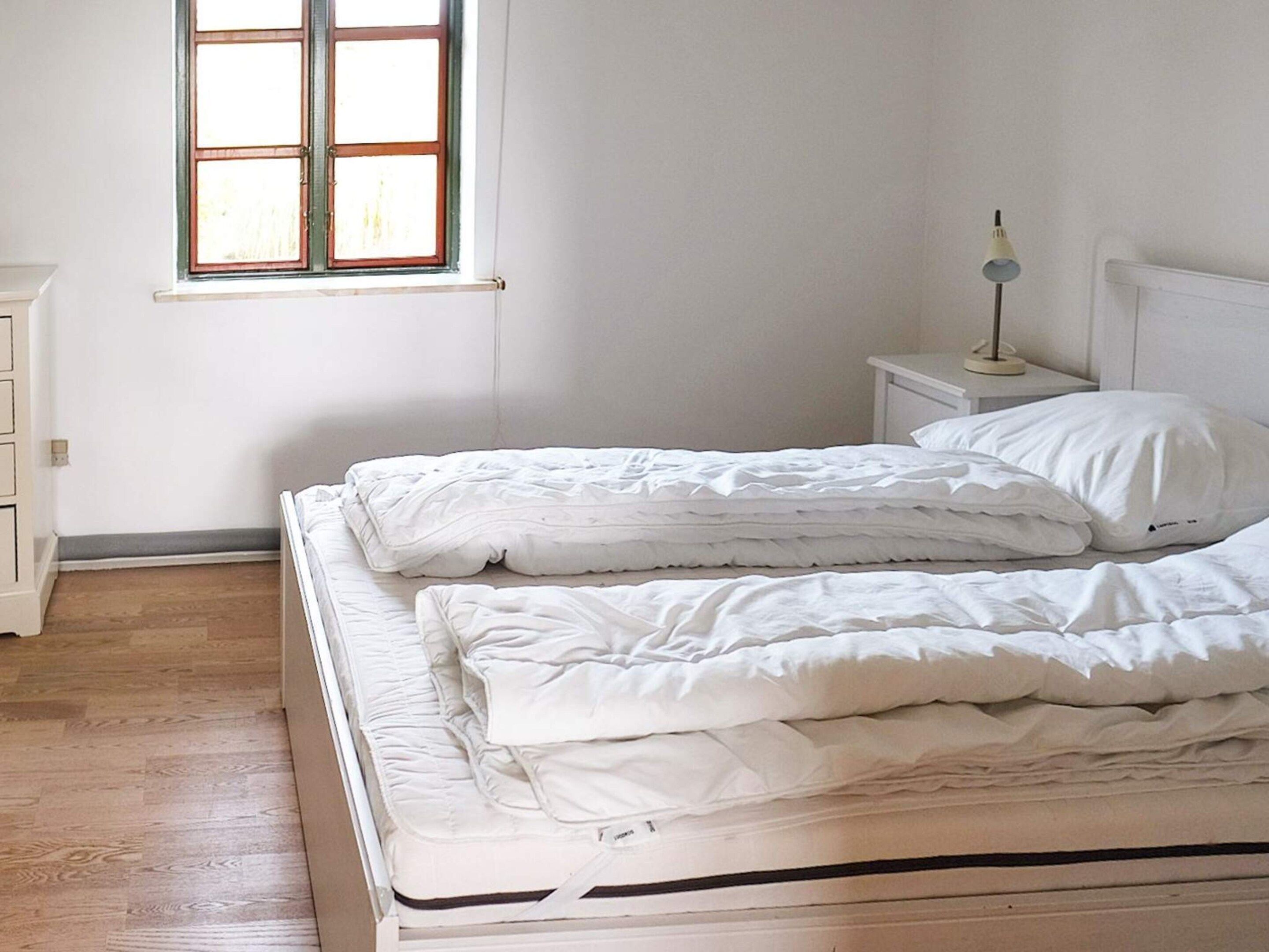 A bedroom with two beds, a nightstand with a lamp, and a window with blinds.
