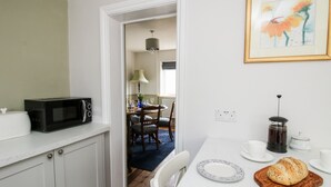 A kitchen with white cabinets, a microwave, a coffee maker, and a bread loaf on a cutting board. - The Ferns (Ludlow)