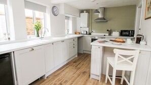 A modern kitchen with white cabinetry, a wooden floor, a clock, and a coffee maker. - The Ferns (Ludlow)