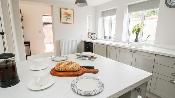 A kitchen with a white countertop, a loaf of bread, a coffee maker, and a window with a view of greenery. - The Ferns (Ludlow)