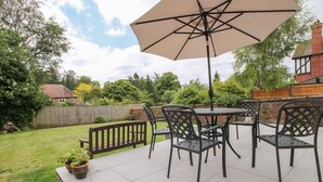 A patio with a table and chairs, a large umbrella, and a brick wall in the background. - The Ferns (Ludlow)