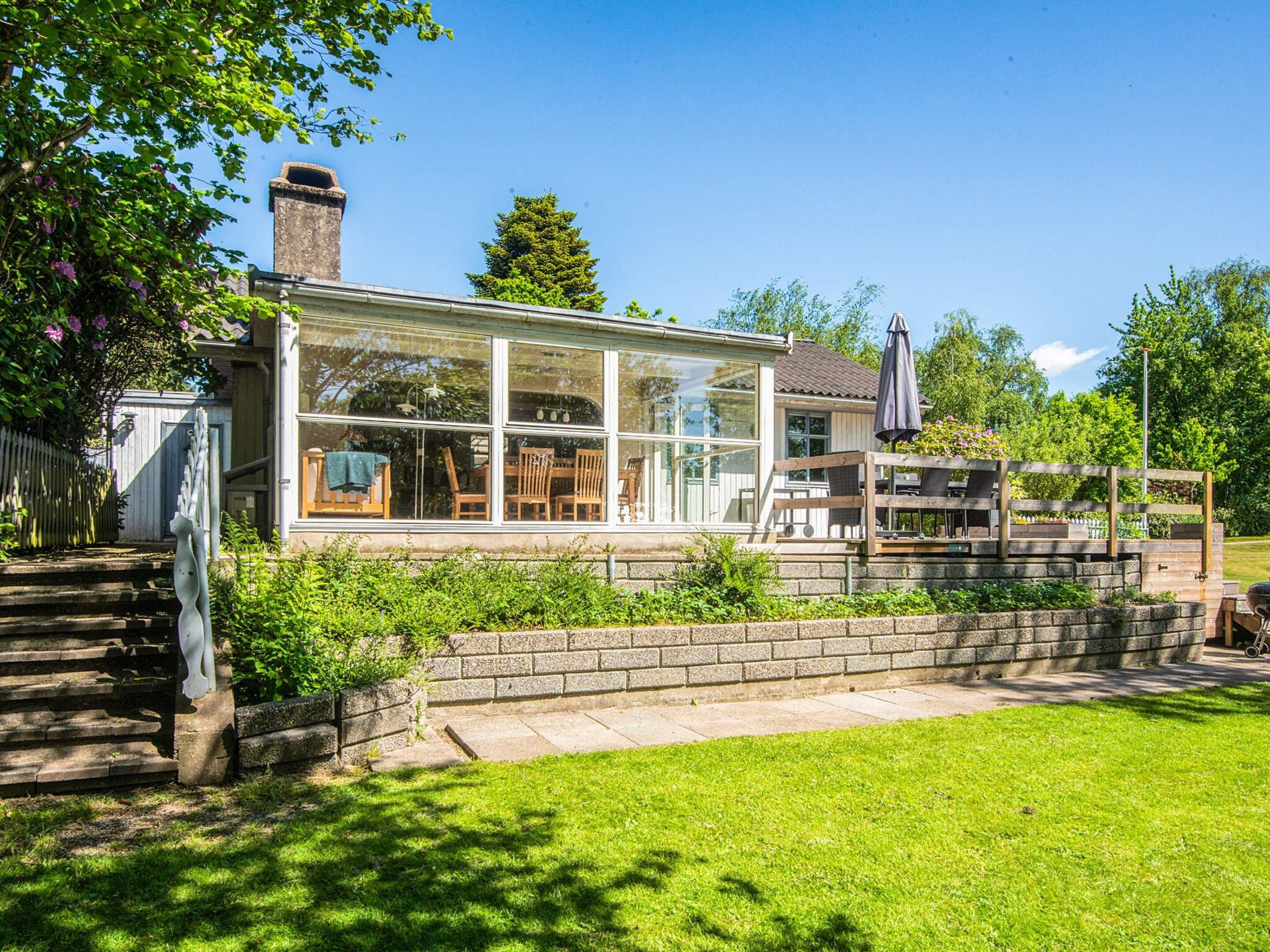 A house with a glass-enclosed porch, a brick wall, and a wooden deck.