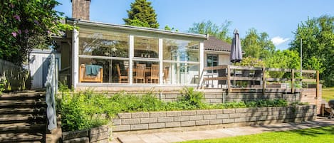 A house with a glass-enclosed porch, a brick wall, and a wooden deck.