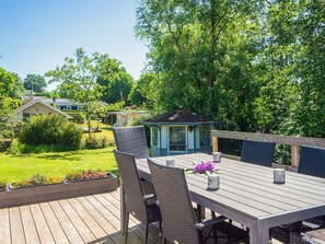 Eine Holzterrasse mit Tisch und Stühlen, ein Gartenpavillon und ein Haus im Hintergrund.