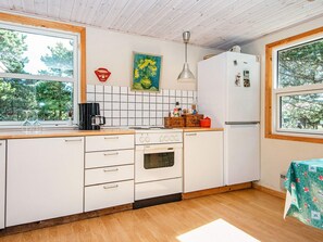 A compact kitchen with white cabinets, a stove, a refrigerator, and a window with a view of trees. - 4 Person Holiday Home in Ebeltoft (Ebeltoft)