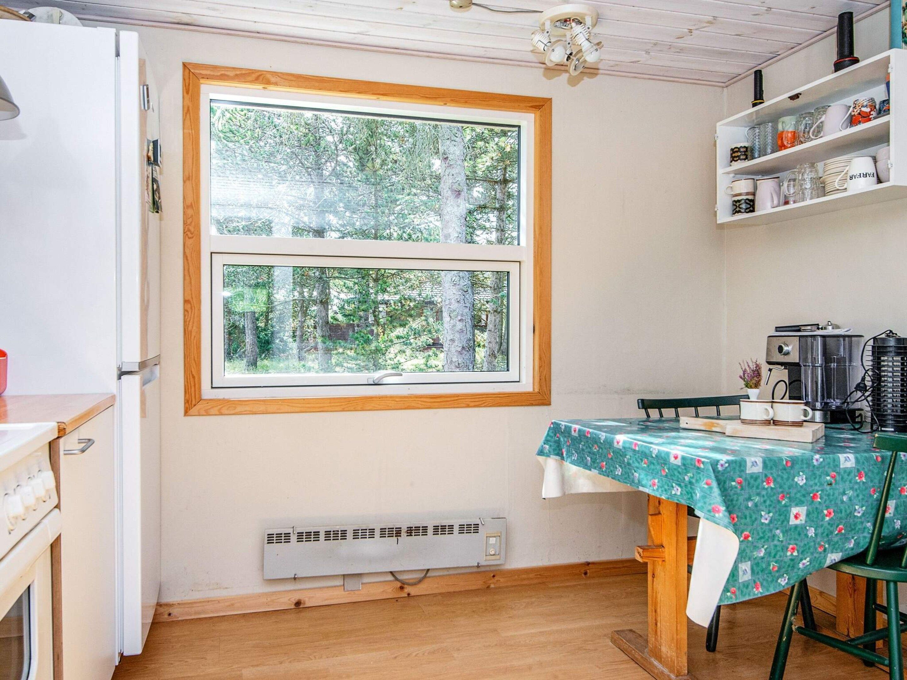 Cozinha compacta com janela, mesa com toalha de mesa florida e cafeteira.