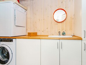 A compact laundry room with a washing machine, a dryer, a wooden cabinet, a mirror, and a small sink with soap dispenser.