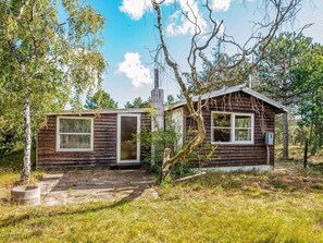 A rustic cabin with a stone pathway leading to the entrance, surrounded by trees and greenery.