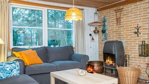 A cozy living room with a fireplace, a sofa, a table, and a large window overlooking a forest. - 4 Person Holiday Home in Ebeltoft (Ebeltoft)
