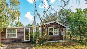 A wooden cabin with a chimney, a window, and a door, surrounded by trees and grass. - 4 Person Holiday Home in Ebeltoft (Ebeltoft)