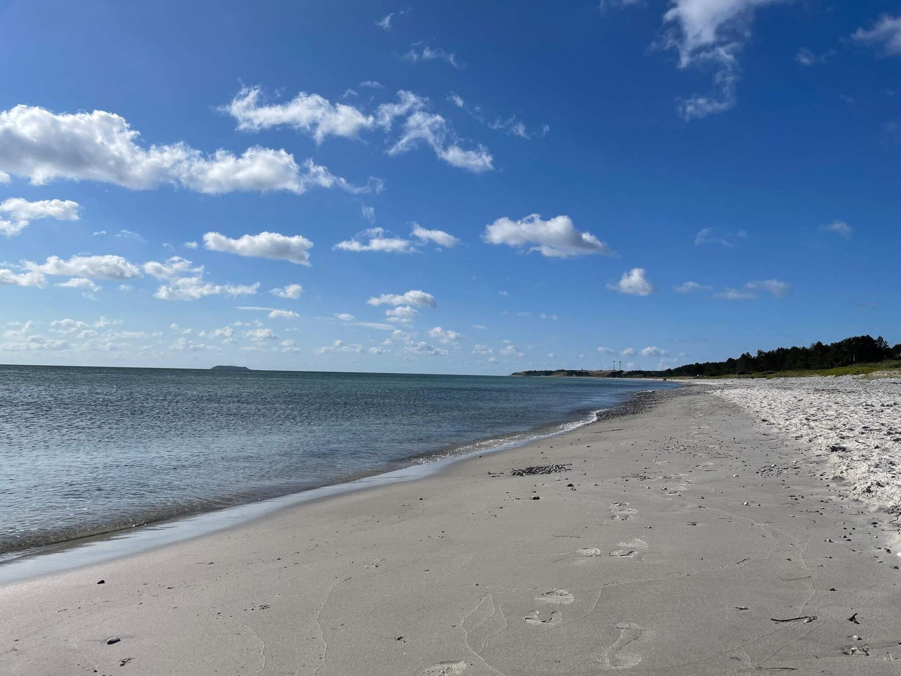 Una playa con cielo despejado, agua tranquila y una orilla arenosa.