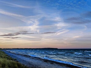A coastal landscape with a beach, ocean, and distant landmass under a cloudy sky.