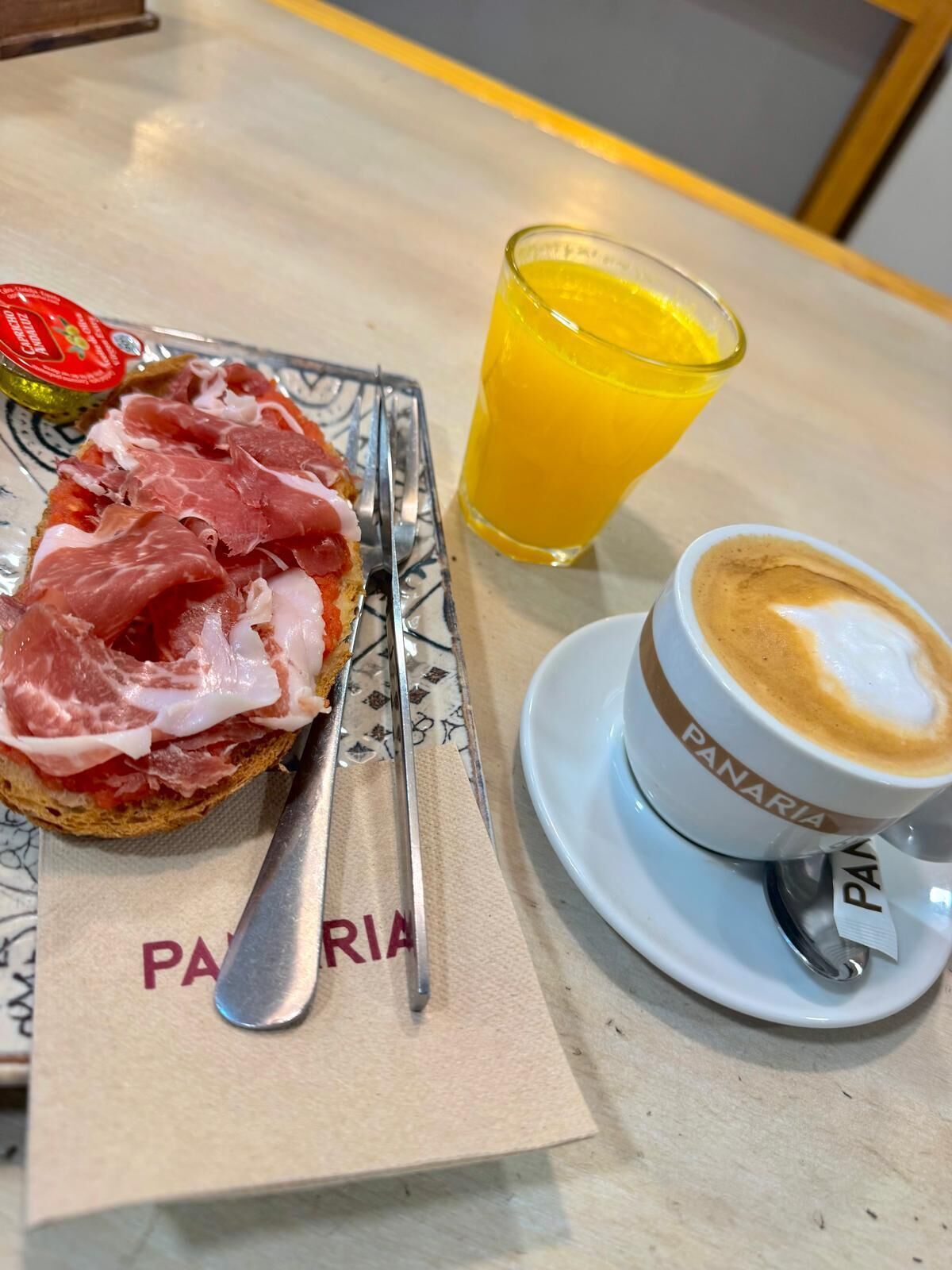 Une table mise pour le petit-déjeuner avec un sandwich, un verre de jus d’orange et une tasse de café.