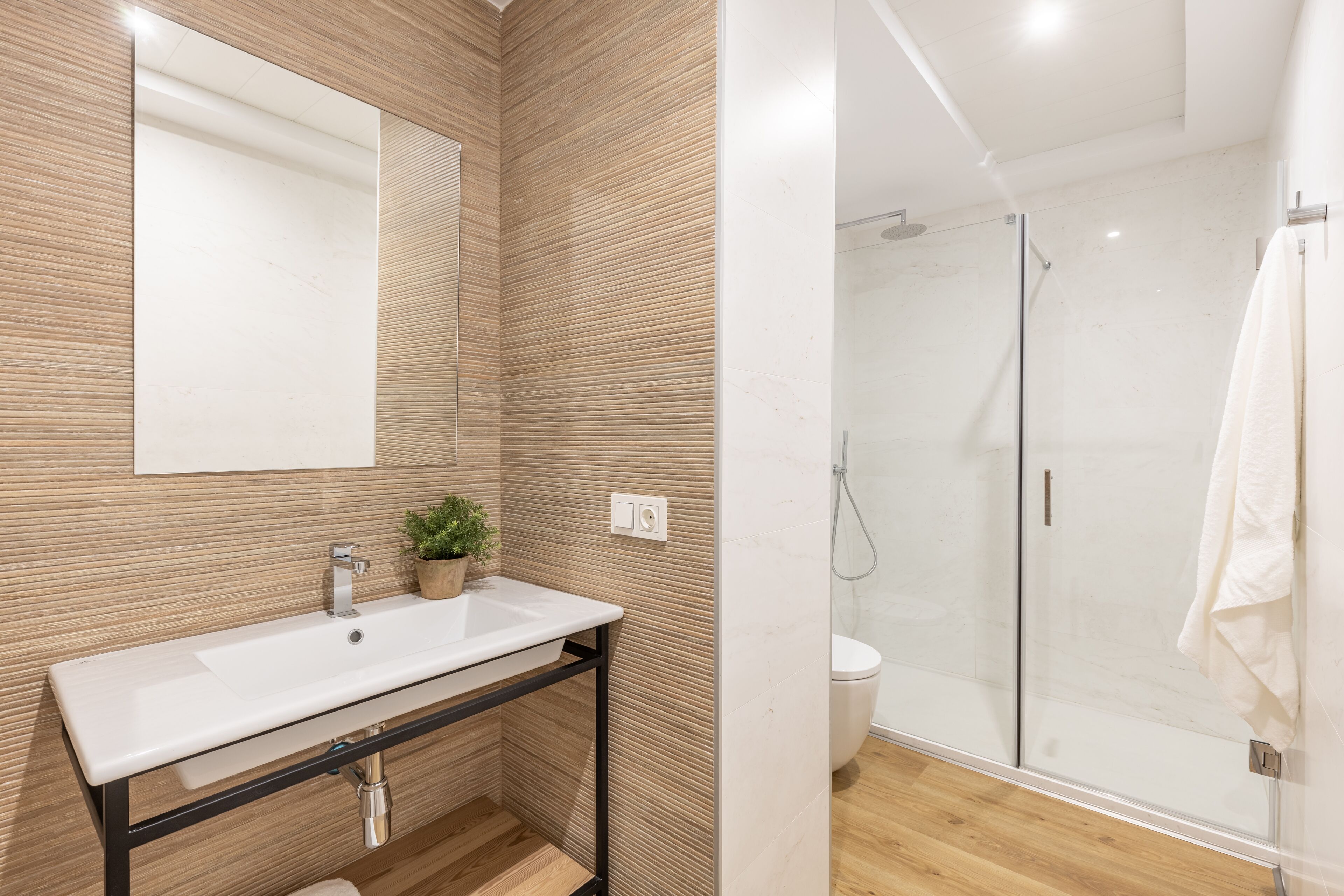 Une salle de bain moderne avec un mur recouvert de panneaux en bois, un lavabo blanc, une petite plante en pot et une cabine de douche en verre.