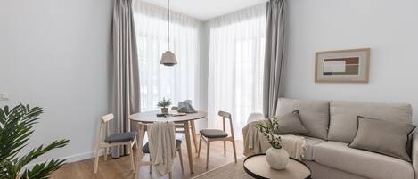 A modern living room with a sofa, dining table, chairs, and a potted plant.