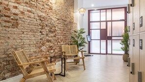 A lobby with a brick wall, wooden chairs, a potted plant, and a wooden cabinet with numbered locks.