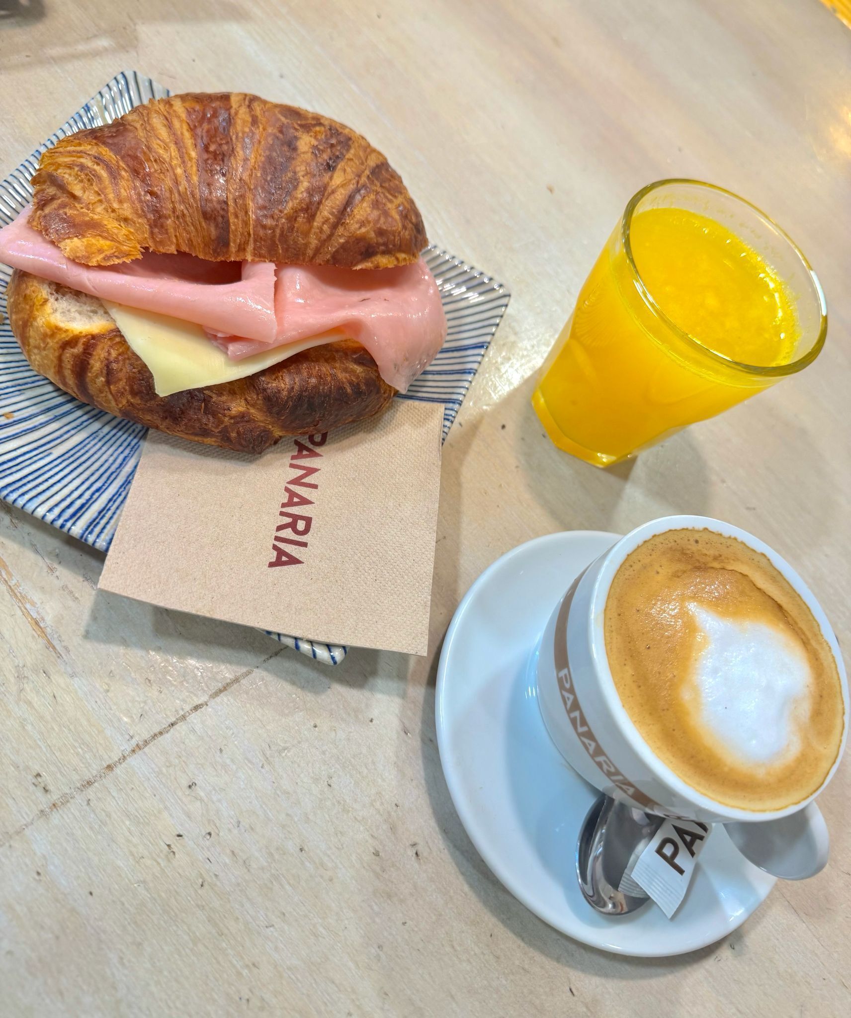 A croissant sandwich with ham and cheese, a glass of orange juice, and a cup of coffee with latte art on a table.