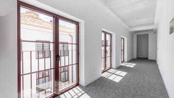 Un couloir doté de grandes portes vitrées donnant sur un balcon, avec un plafond blanc et un sol recouvert d’une moquette grise.