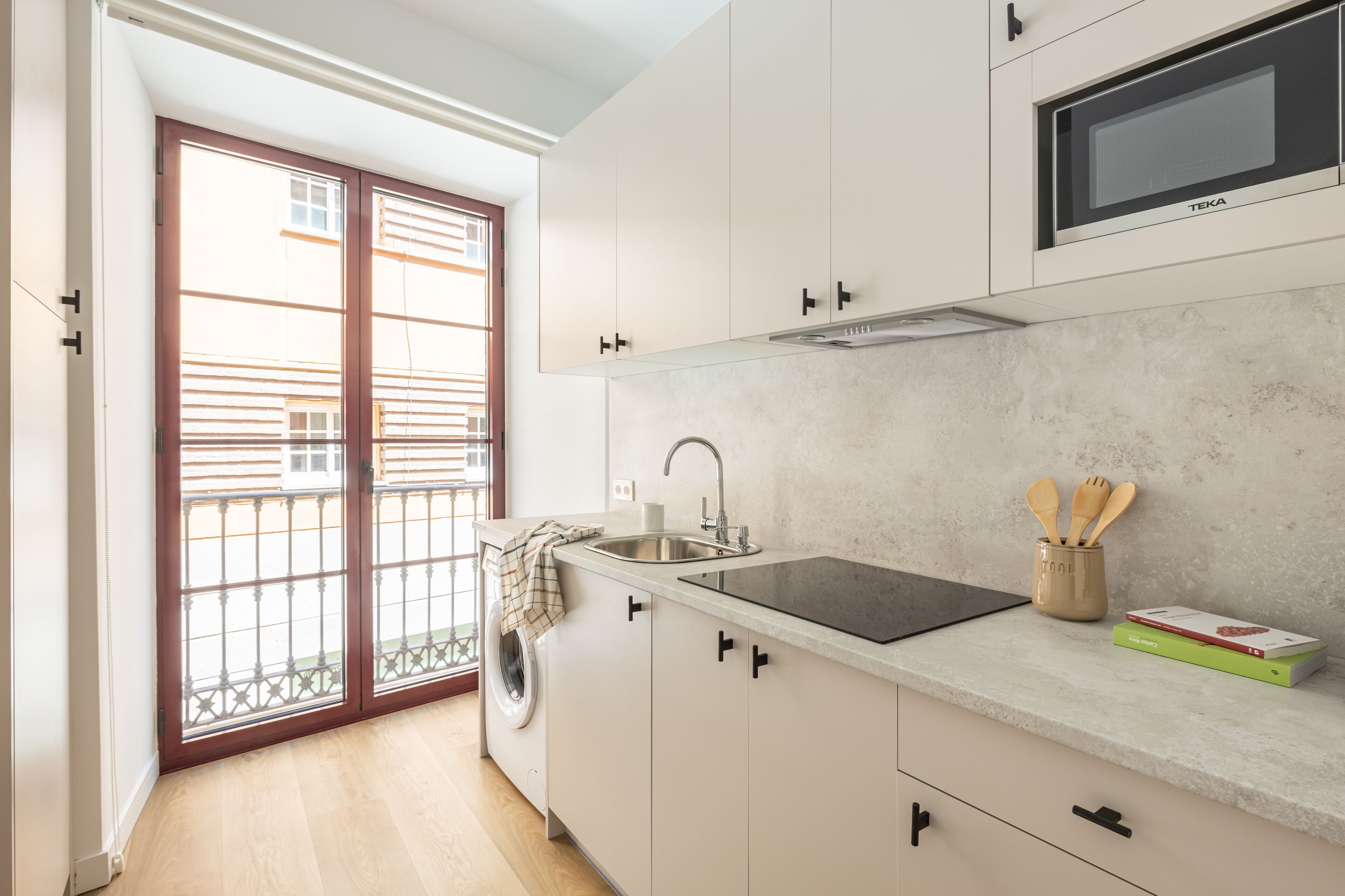 Una cucina moderna con forno a microonde integrato, lavandino e finestra con vista su un balcone.