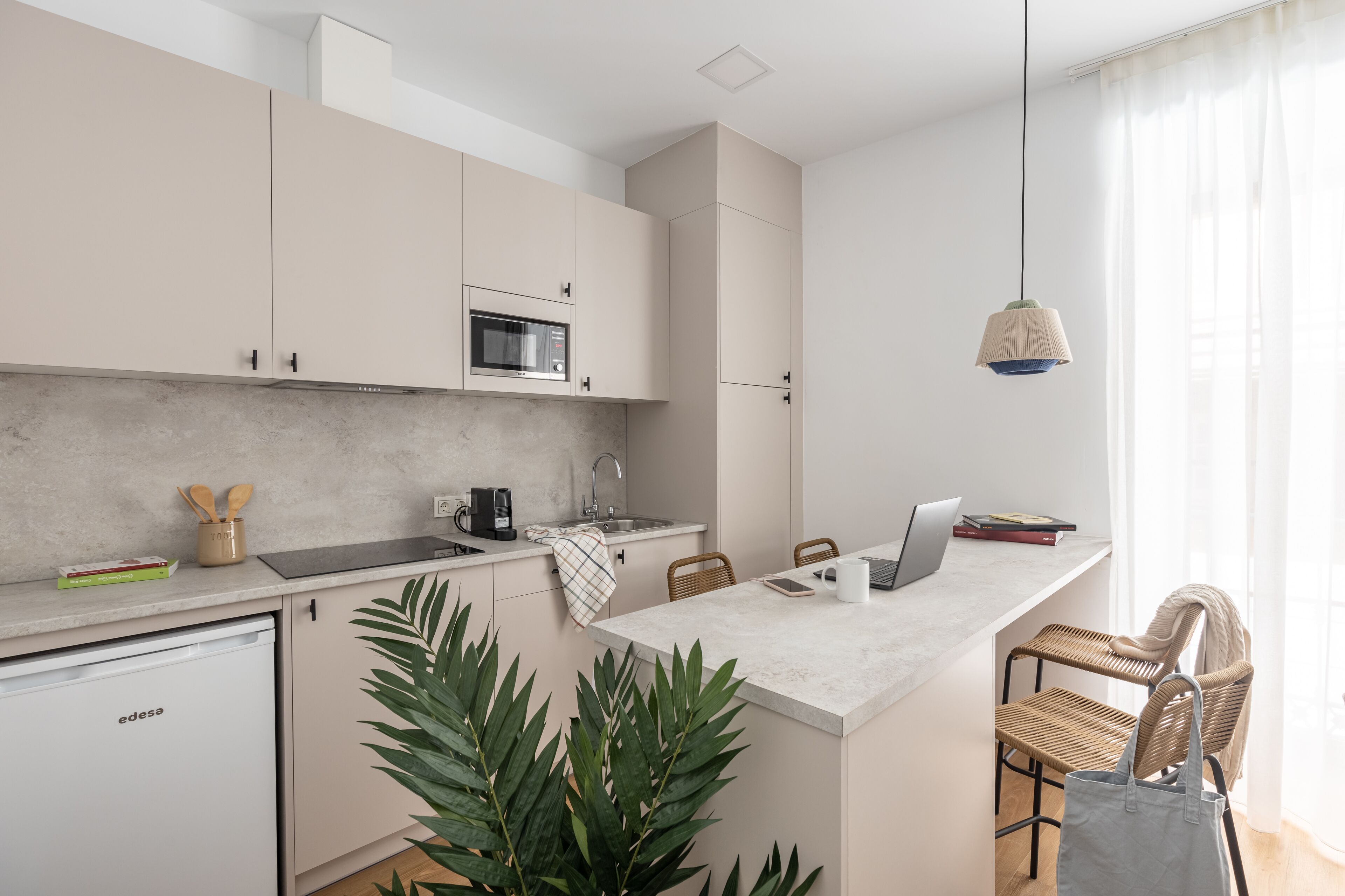 A modern kitchen with a built-in microwave, a coffee maker, and a small island with a laptop.