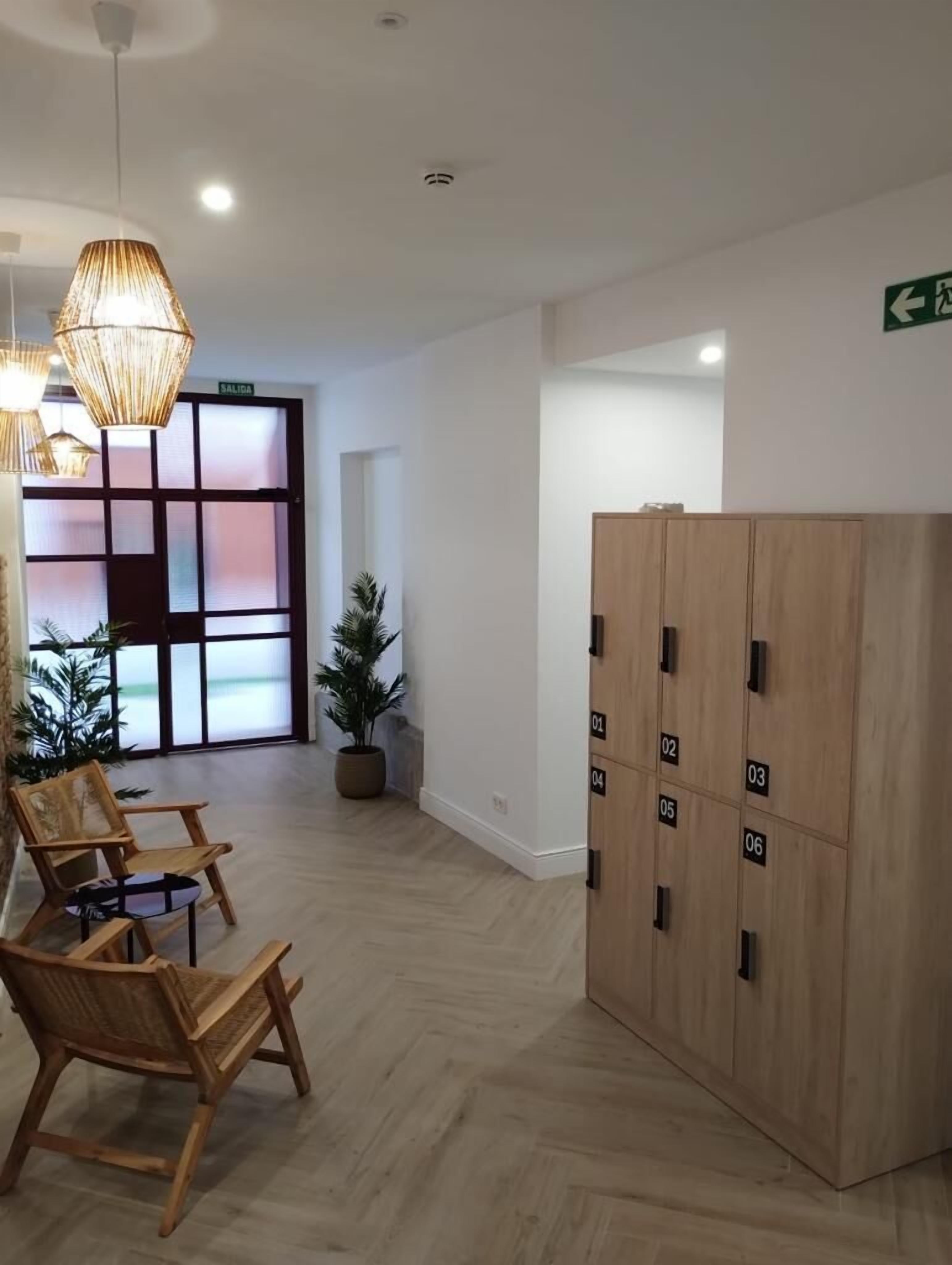 Een ontvangstruimte met houten stoelen, een potplant, een houten kast met genummerde kluisjes en een deur met geëtste glaspaneel.